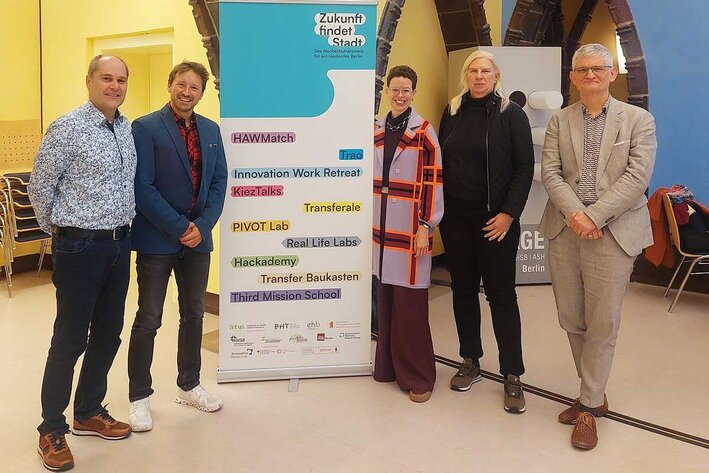 Fünf Personen posieren mit einer Stellwand in der Mitte