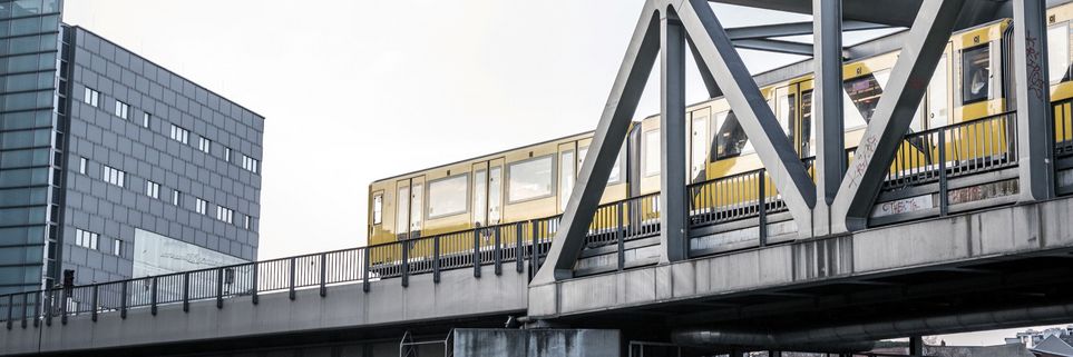 Brücke, auf der eine gelbe U-Bahn fährt. Dahinter ein modernes Hochhaus.