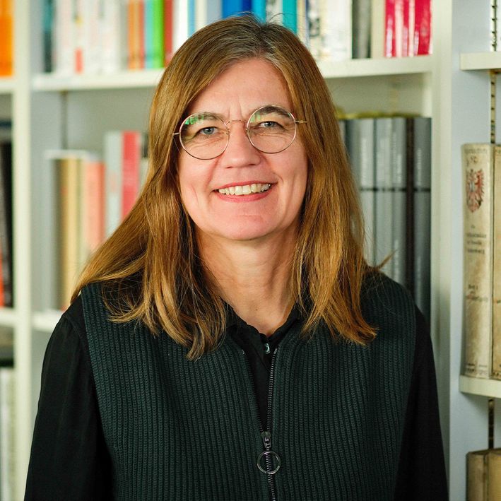 Portraitbild einer Frau mit Brille vor einem Bücherregal.