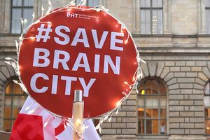 Schild mit der Aufschrift #SaveBrainCity vor einem Gebäude