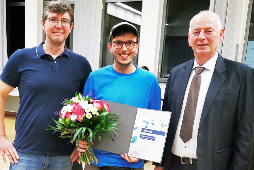 Der Preisträger posiert gemeinsam mit zwei weiteren Personen mit seiner Urkunde und einem Blumenstrauß