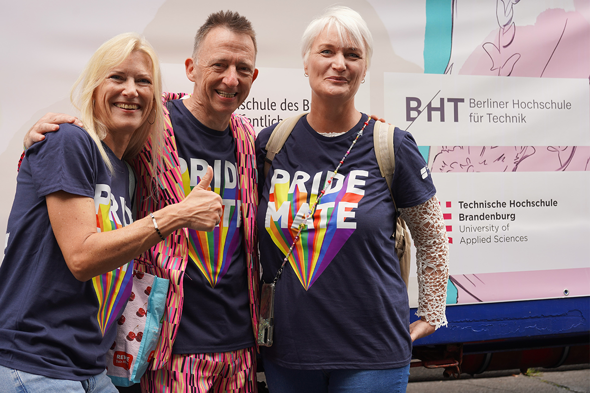 Drei lächelnde Personen in T-Shirts mit der Aufschrift „Pride Mate“.