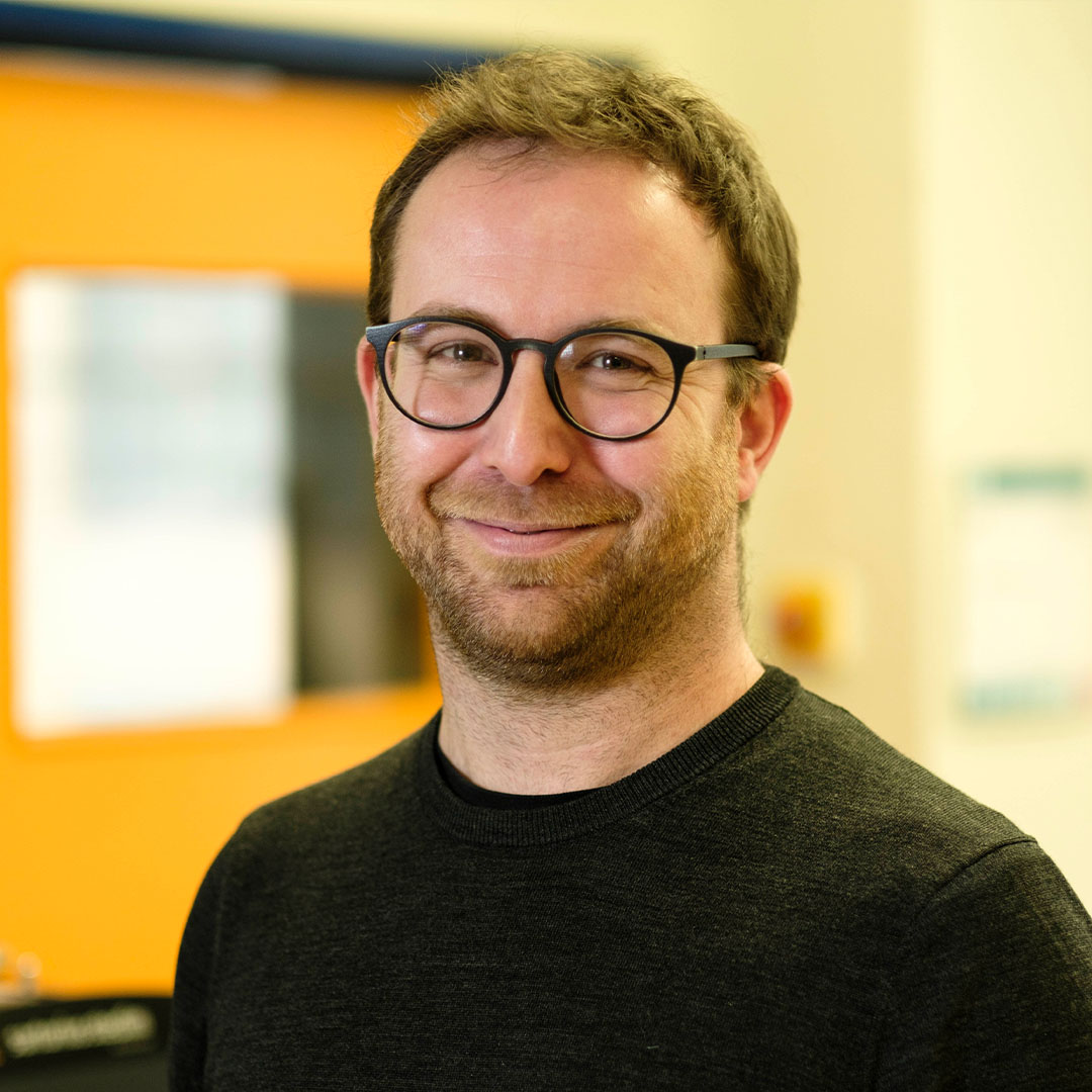 Portraitbild eines Mannes mit Brille und schwarzem Pullover.